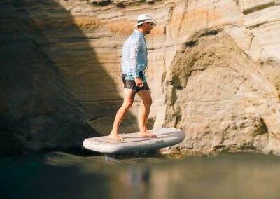 Man paddleboarding near rocky cliffs.